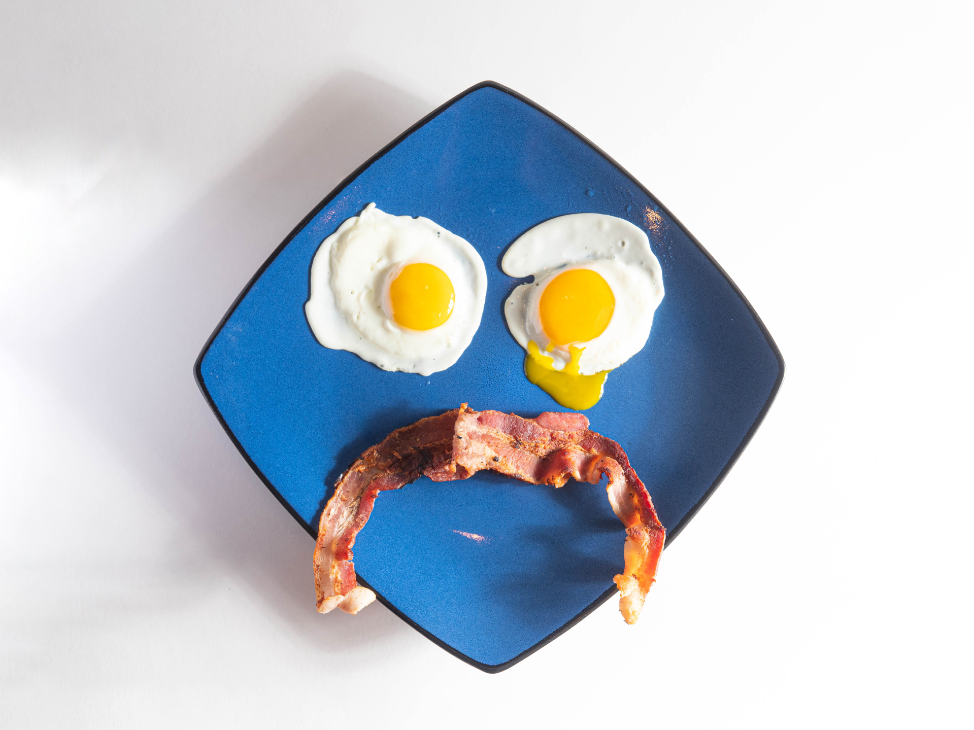 Two eggs sunny side up with bacon in a frown shape on a blue plate